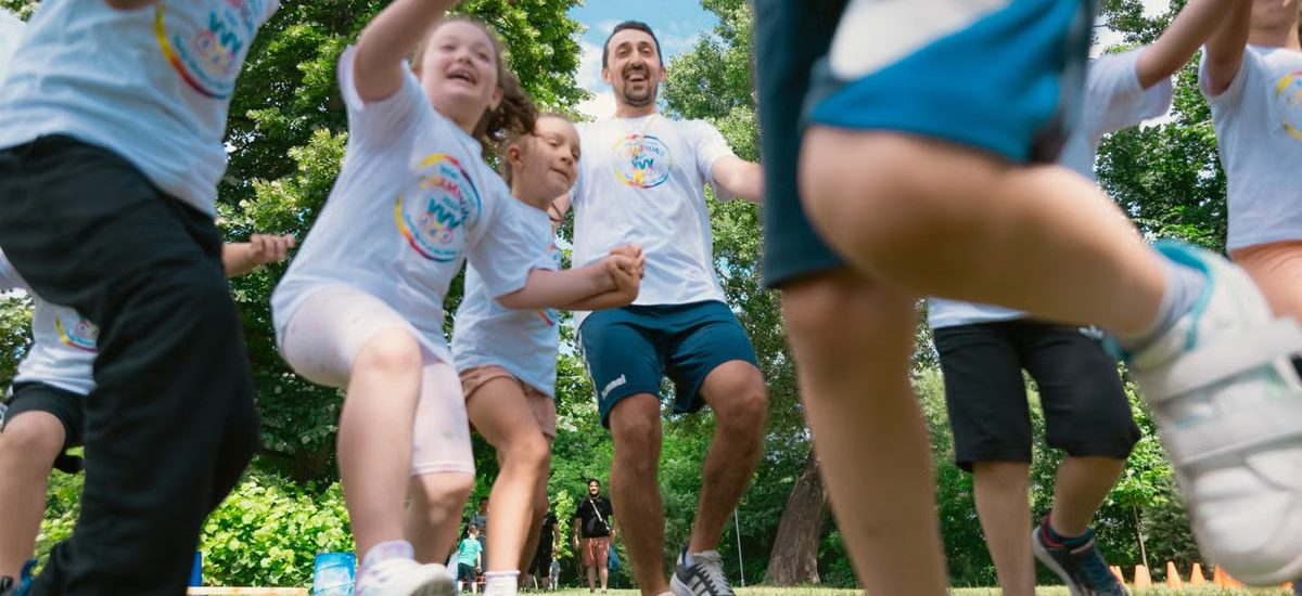 Joyful group of children and adult engaging in playful activities in a sunny park setting.