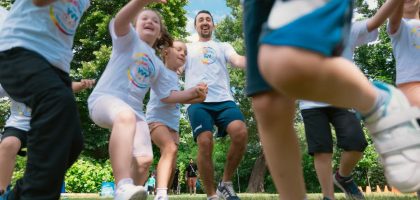 Joyful group of children and adult engaging in playful activities in a sunny park setting.