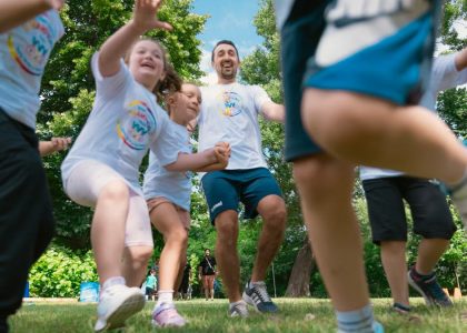 Joyful group of children and adult engaging in playful activities in a sunny park setting.
