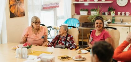 Elderly residents and caregivers enjoying a meal and conversation in a cheerful dining space.