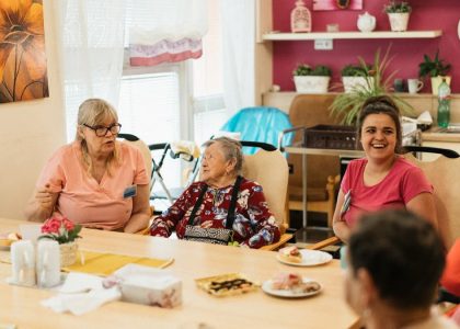 Elderly residents and caregivers enjoying a meal and conversation in a cheerful dining space.